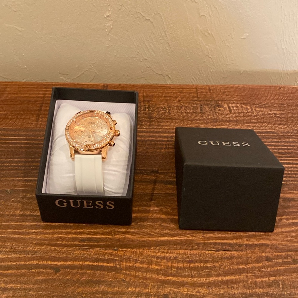 Rose gold watch with diamond like stones and a white wrist band.